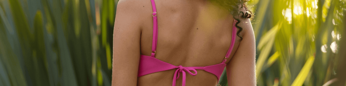 Model wearing a bright pink Nelly bikini set on a tropical beach, showcasing a flattering and supportive fit in sustainable swimwear.